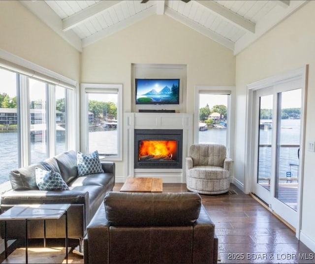 living area with baseboards, vaulted ceiling with beams, a water view, a lit fireplace, and hardwood / wood-style flooring
