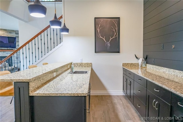 bar featuring hanging light fixtures, light wood-type flooring, a sink, baseboards, and stairs