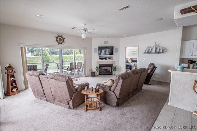 living room featuring visible vents, light carpet, a fireplace, ceiling fan, and light tile patterned floors