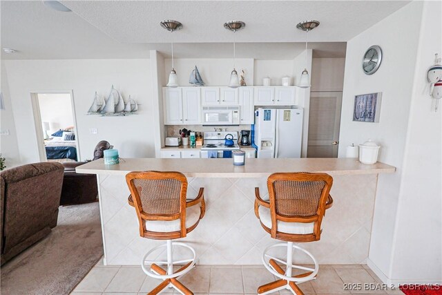 kitchen featuring pendant lighting, a breakfast bar, white appliances, light countertops, and white cabinetry