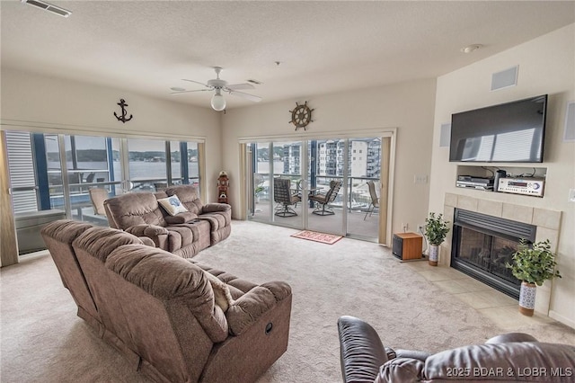 living area with visible vents, a ceiling fan, light carpet, and a tile fireplace