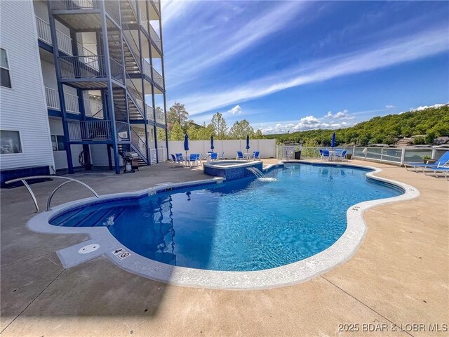 view of pool with fence, stairs, a pool with connected hot tub, and a patio area