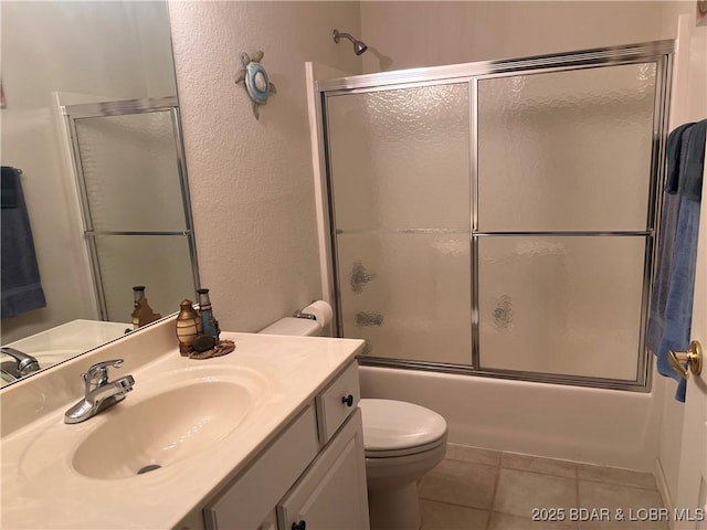 bathroom with shower / bath combination with glass door, a textured wall, vanity, toilet, and tile patterned floors