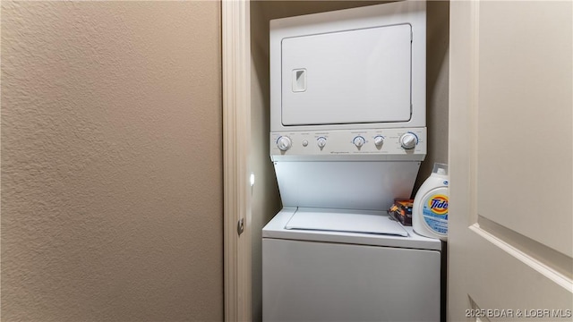 laundry room featuring laundry area, a textured wall, and stacked washing maching and dryer