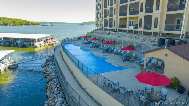 community pool with fence, a water view, cooling unit, and a patio area
