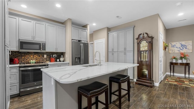 kitchen with wood tiled floor, tasteful backsplash, a sink, baseboards, and stainless steel appliances