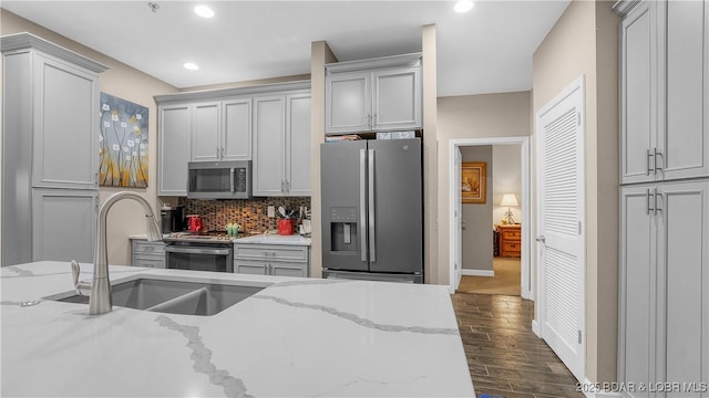 kitchen featuring dark wood-type flooring, light stone counters, a sink, backsplash, and stainless steel appliances