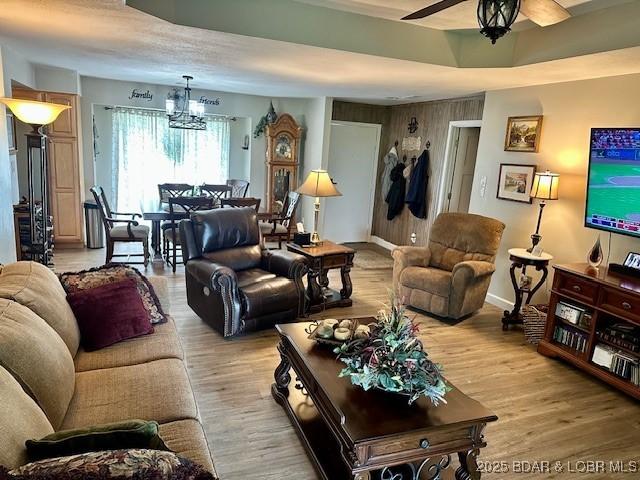 living area with baseboards, light wood-style flooring, and ceiling fan with notable chandelier