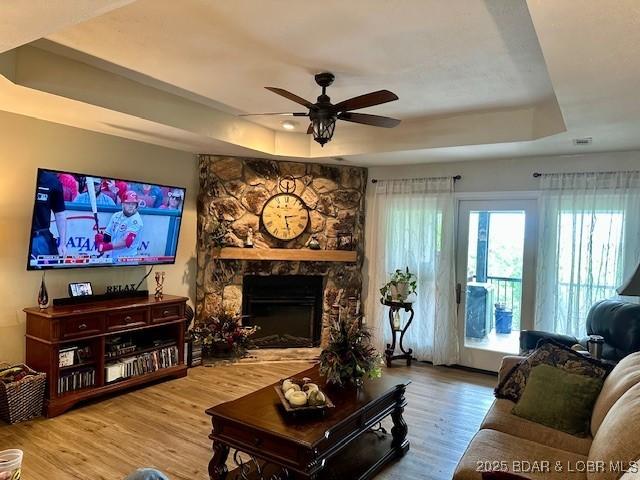 living room featuring a raised ceiling, ceiling fan, wood finished floors, and a fireplace