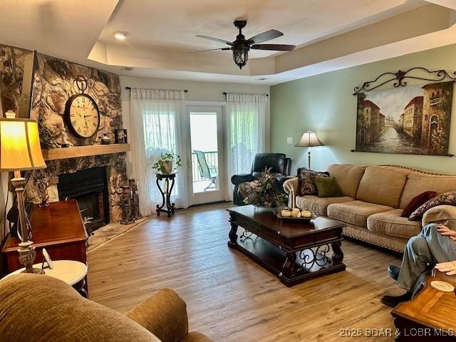 living room featuring a raised ceiling, ceiling fan, and light wood-type flooring