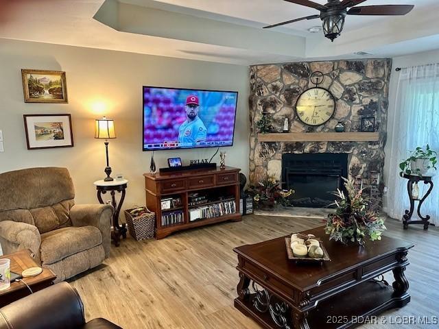 living room featuring a ceiling fan, a raised ceiling, wood finished floors, and a fireplace