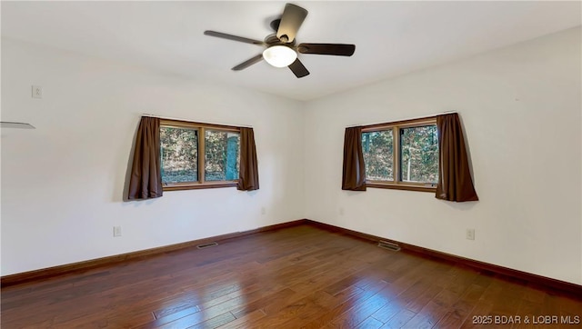 empty room featuring a ceiling fan, dark wood-type flooring, and visible vents