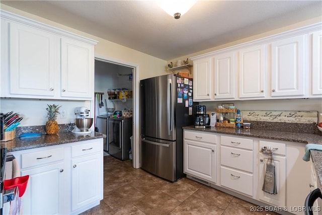 kitchen with freestanding refrigerator, dark stone countertops, washing machine and dryer, and white cabinets