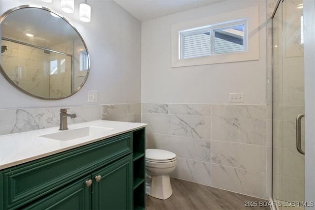 full bath with a stall shower, vanity, tile walls, and toilet