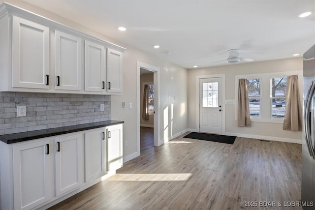 kitchen featuring white cabinets, dark countertops, ceiling fan, baseboards, and tasteful backsplash