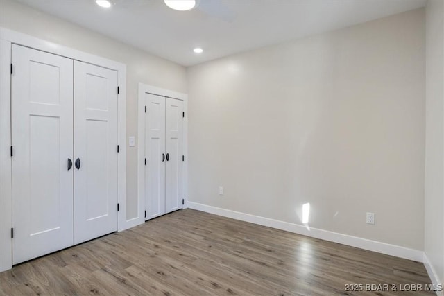 unfurnished bedroom with baseboards, recessed lighting, multiple closets, and wood finished floors