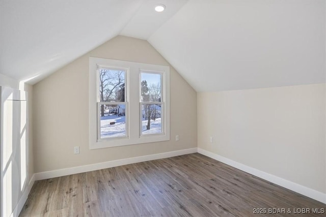 additional living space with baseboards, wood finished floors, and vaulted ceiling