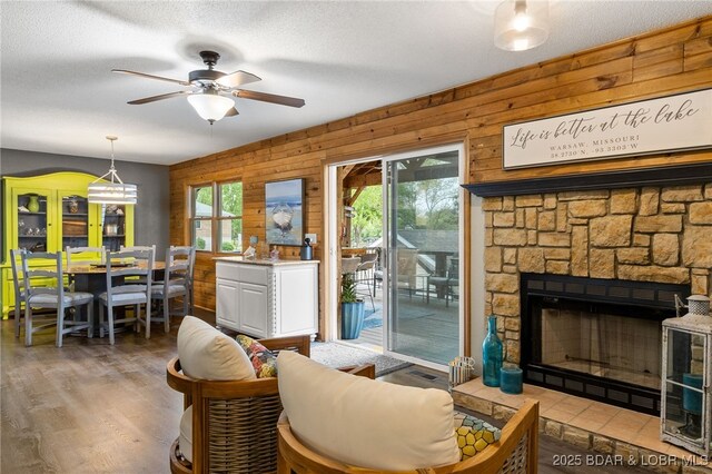 20168 Lost Valley Rd, Warsaw, MO 65355 - living room with a ceiling fan, wood finished floors, a stone fireplace, wood walls, and a textured ceiling