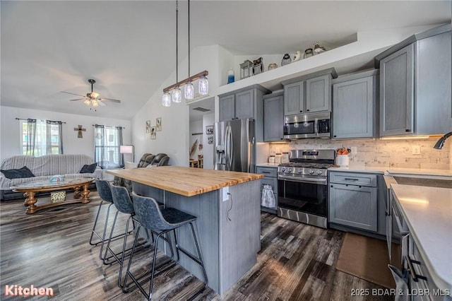 kitchen featuring appliances with stainless steel finishes, a breakfast bar area, butcher block countertops, dark wood finished floors, and lofted ceiling