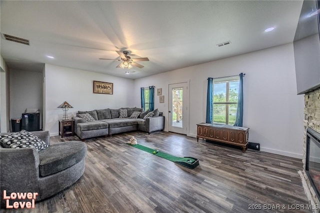 living area with visible vents, ceiling fan, wood finished floors, and a stone fireplace