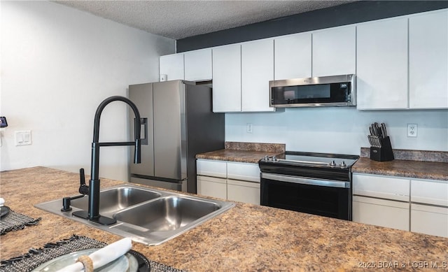 kitchen featuring a sink, a textured ceiling, white cabinetry, dark countertops, and appliances with stainless steel finishes