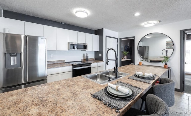 kitchen with a sink, a breakfast bar, a textured ceiling, white cabinets, and appliances with stainless steel finishes
