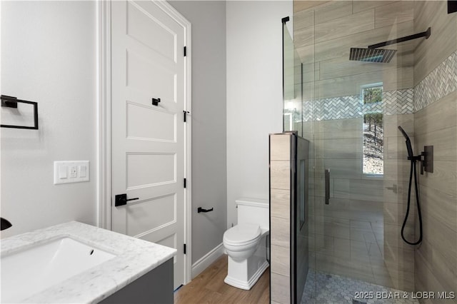 bathroom featuring vanity, toilet, wood finished floors, and a stall shower