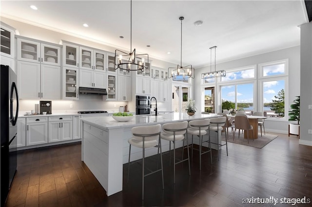 kitchen with freestanding refrigerator, a notable chandelier, white cabinets, under cabinet range hood, and gas cooktop