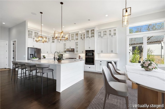 kitchen with stainless steel fridge with ice dispenser, dobule oven black, dark wood-type flooring, light countertops, and a chandelier