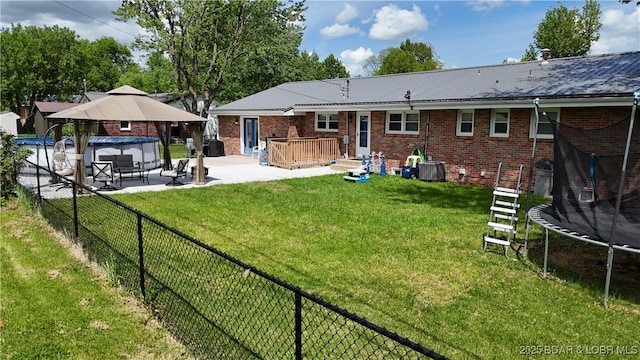 back of house with a trampoline, a gazebo, a fenced backyard, a yard, and a patio area