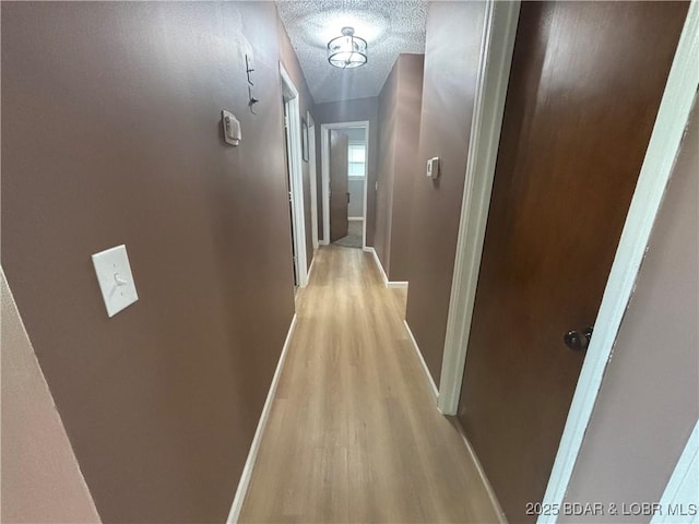 hall featuring a textured ceiling, baseboards, and light wood-style floors
