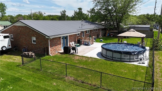 rear view of house featuring a gazebo, brick siding, a yard, a fenced backyard, and a covered pool
