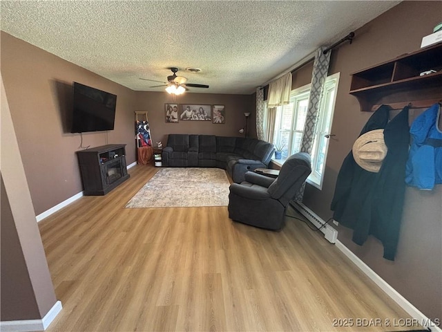 living area with a ceiling fan, light wood-style flooring, a textured ceiling, a baseboard heating unit, and baseboards