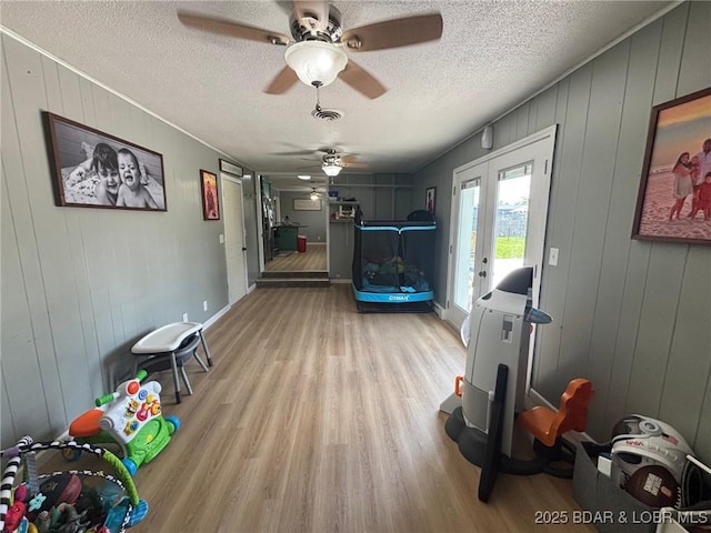 rec room with light wood-type flooring, visible vents, baseboards, a textured ceiling, and ceiling fan