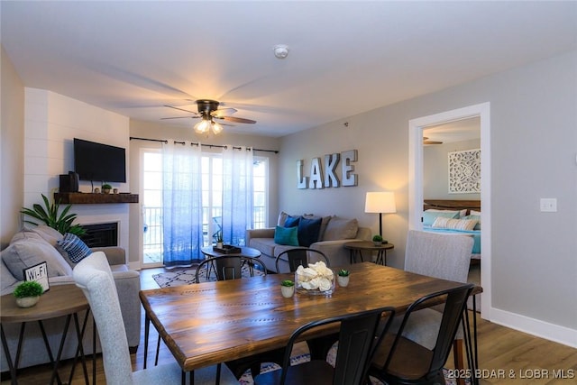 dining area with a ceiling fan, baseboards, a fireplace, and wood finished floors