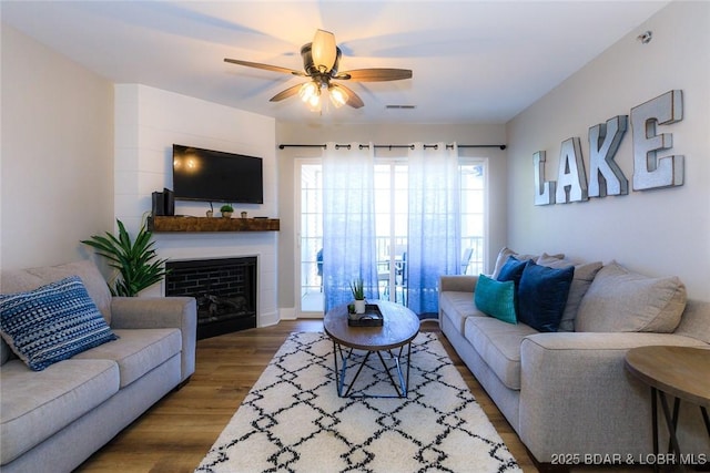 living area featuring a fireplace, ceiling fan, visible vents, and wood finished floors