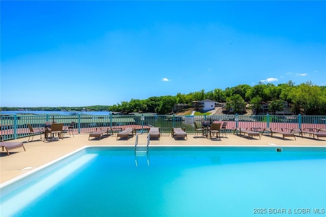 community pool featuring a water view, a patio, and fence