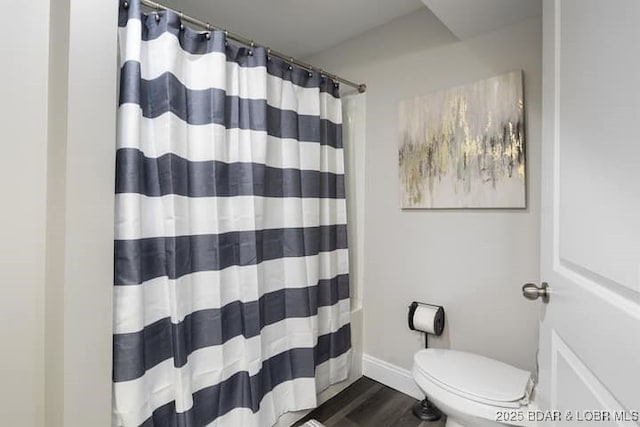 bathroom with toilet, curtained shower, baseboards, and wood finished floors