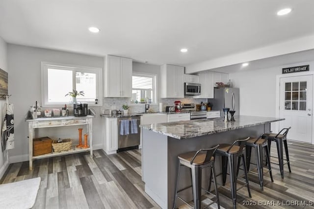 kitchen featuring stone counters, dark wood-style flooring, a kitchen breakfast bar, stainless steel appliances, and white cabinets