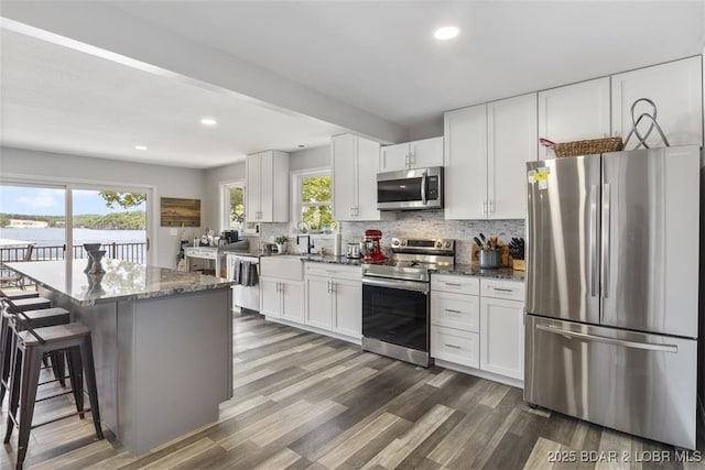 kitchen with dark stone counters, a kitchen breakfast bar, dark wood-style flooring, appliances with stainless steel finishes, and decorative backsplash