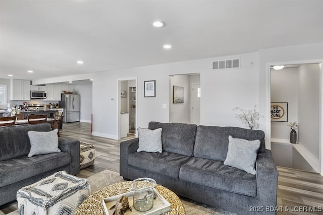 living room featuring light wood-type flooring, visible vents, baseboards, and recessed lighting