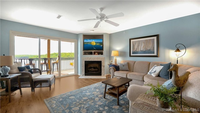living area with a premium fireplace, visible vents, a ceiling fan, and wood finished floors