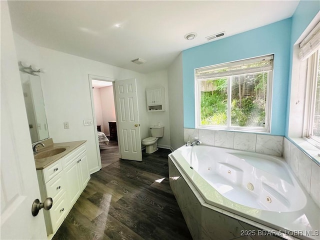 ensuite bathroom featuring toilet, wood finished floors, a jetted tub, visible vents, and vanity