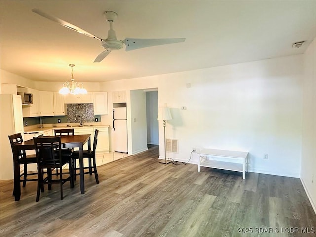 dining area with light wood-style flooring, ceiling fan with notable chandelier, baseboards, and visible vents