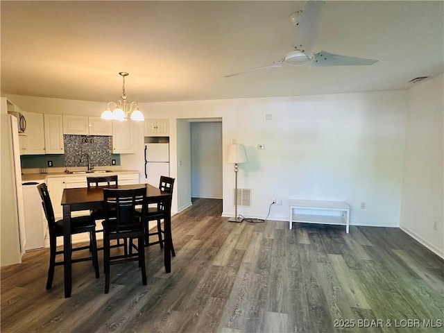 dining area featuring baseboards, ceiling fan with notable chandelier, visible vents, and dark wood-type flooring