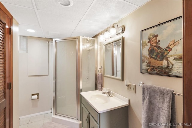 full bathroom featuring a shower stall, tile patterned floors, vanity, baseboards, and a paneled ceiling