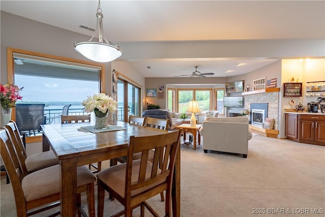 dining space with light colored carpet, visible vents, a fireplace, and ceiling fan