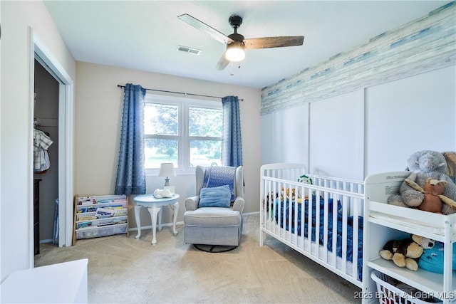 carpeted bedroom with a crib, baseboards, a ceiling fan, and visible vents