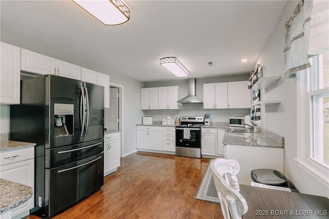 kitchen with stainless steel appliances, wall chimney range hood, wood finished floors, white cabinetry, and light stone countertops