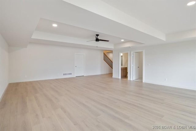 unfurnished living room featuring a tray ceiling, recessed lighting, stairway, and light wood-style flooring